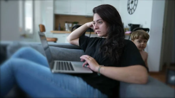Woman browsing internet with laptop computer sitting on couch at home. Person looking at screen. Modern lifestyle