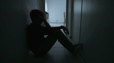 Depressed man sitting on floor. Sad unhappy person holding his forehead suffering from mental illness. Depression concept
