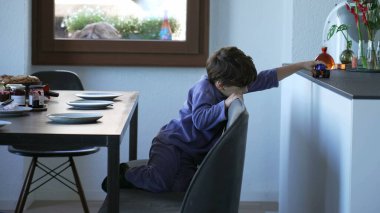 One cute little boy playing with car toy in breakfast table. Child waiting for family to arrive in the morning. Kid playing by himself wearing pajama. Authentic domestic lifestyle