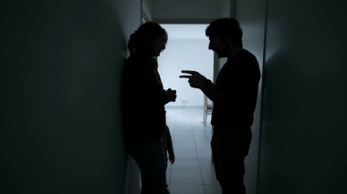 Couple discussing relationship with child in the middle. Silhouettes of man and woman conversation standing at home corridor. Parents talking