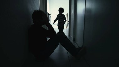 Depressed father being consoled by son sitting in corridor in silhouette. Child hugging sad parent during crisis
