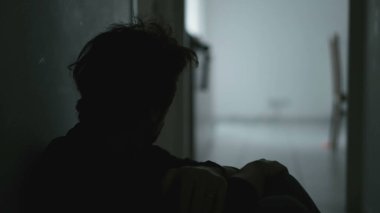 Sad unhappy man sitting on floor holding his forehead while having mental pain. Depressed person in dark corridor with low light environment. Dramatic scene