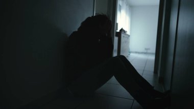 One anxious depressed woman covering face in despair sitting at home in the dark. Person suffering alone in corridor feeling shame and regret