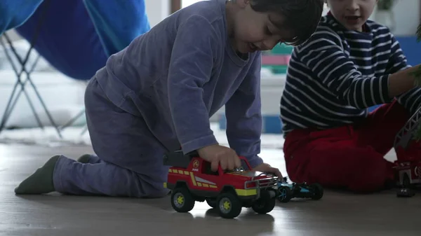 Child playing with firetruck toy car on floor. Little boy wearing pajama plays with toys indoors during Christmas day