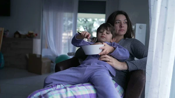 Cute child leaning on mother body in the morning. Domestic lifestyle of kid laying on parent lap wearing pajamas