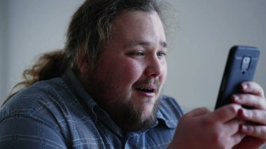 One happy man cheering success in front of smartphone device. Person celebrates GOOD news notification on phone screen