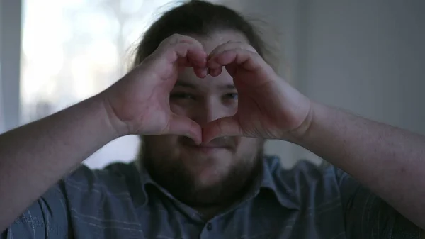 One young chubby man doing heart symbol with hands indoors. Happy person signaling love and empathy concept