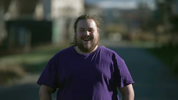 One chubby joyful young man laughing and smiling outside. Portrait of a happy casual person standing outdoors. Tracking shot
