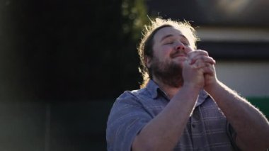 Spiritual young man praying to GOD outdoors in sunlight. A male overweight caucasian person with hands clenched in prayer. Hope and Faith concept