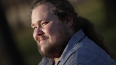 Relaxed young man sitting at park in nature feeling happy. Contemplative person smiling