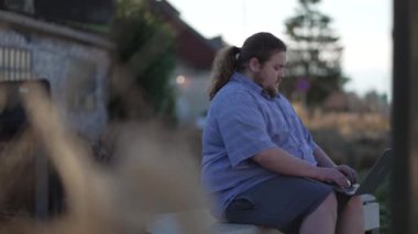 One young man using laptop outdoors sitting at bench using modern technology remotely. Freelancer doing remote work typing on computer