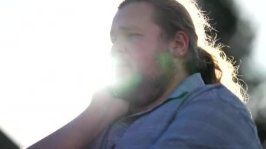 Frustrated young man feeling anxiety and worry standing outdoors in sunlight. Pensive preoccupied emotion of a chubby man feeling regret