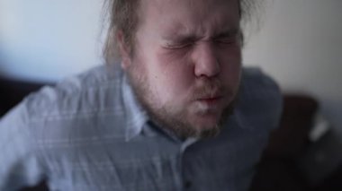 One fat guy having back pain when getting up from couch indoors. A sedentary overweight man suffering from physical injury backache. Person close up face hurting