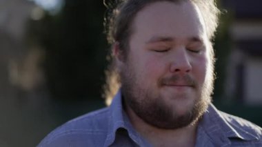 One meditative overweight young man closing eyes in contemplation outdoors in sunlight. Peaceful person feeling serene and calm during meditation session