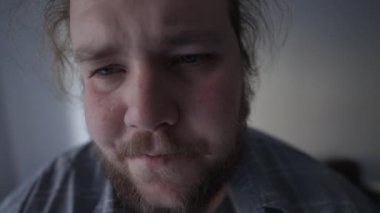 Kalp rahatsızlığı olan biri kalp çarpıntısı geçiriyor. Kanepeye oturmuş göğsünde basınç olan endişeli, kilolu genç bir adam.