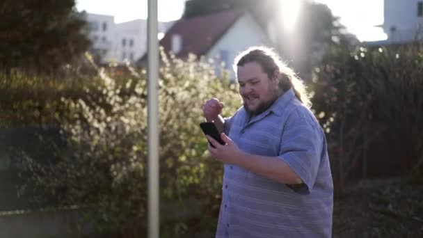 Ein Begeisterter Mann Feiert Seine Erfolgreiche Bewerbung Während Draußen Auf — Stockvideo