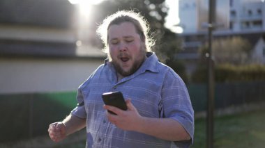 One enthusiastic man celebrating successful job application while walking outdoors in street. Male caucasian person receiving positive message confirmation feeling excited and happy