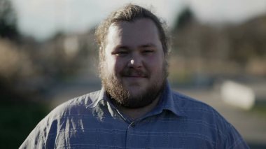 Portrait of a chubby young man walking forward outside in city looking at camera smiling