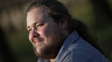 Relaxed young man sitting at park in nature feeling happy. Contemplative person smiling