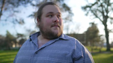 Joyful young man walking outside at park in slow motion. Portrait of a happy overweight 20s guy walks outdoors in nature