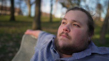 One relaxed young man seated at park bench in contemplation. Happy restful person enjoying nature during sunset time