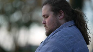 Close up young man typing on laptop sitting outside at park. One chubby casual male caucasian person working remotely in front of computer screen outdoors