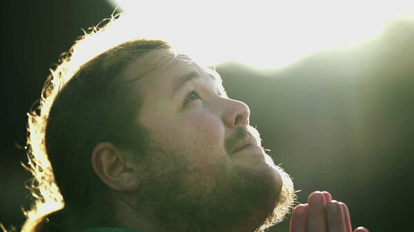 Spiritual young man praying to GOD outdoors in nature. Profile face close up of a chubby casual male person in prayer feeling the presence of a higher power. HOPE and FAITH concept