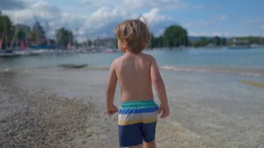 One small boy walking at beach shirtless. Cute child enjoying summer day observing surroundings