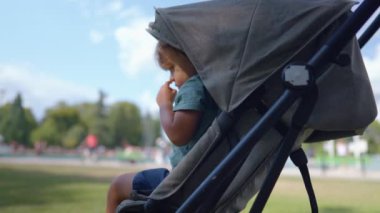 Child inside stroller outside in park. One little boy resting outdoors sitting in baby carriage