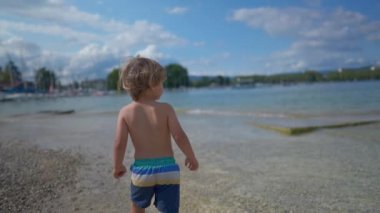 Child walking at beach shore during summer day. One small boy enjoying holiday vacations during sunny day