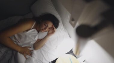 Woman turning bedside light ON in the middle of the night. Female person getting up early in the morning before sunrise