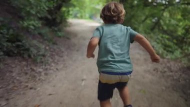 Forest Park 'ın dışında koşan aktif küçük bir çocuğun arkasında. Çocuk yaz tatillerinde dışarıda koşuyor.