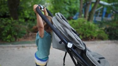 Cute little boy pushing stroller chair outside. Child pushes carriage during weekend family activity at park. kid helping with baby carriage