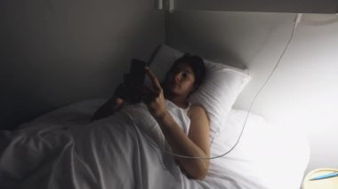 Yatakta uzanmış, gece uyumadan önce akıllı telefon ekranına bakıyordu.