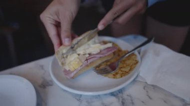 Close up hand preparing sandwich with ham and brie cheese on plate. Person making food on the go snack