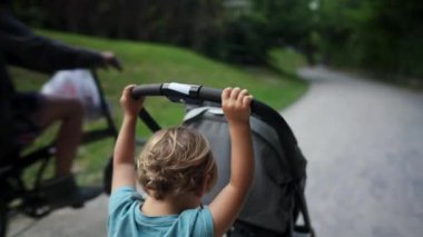 Cute little boy pushing stroller chair outside. Child pushes carriage during weekend family activity at park. kid helping with baby carriage