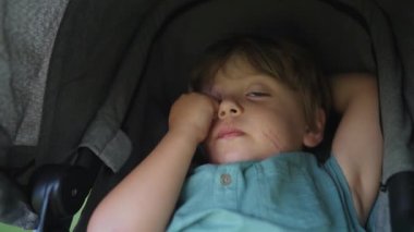 Yorgun küçük bir çocuk bebek arabasının içinde uyuduktan sonra uyandı. Kalkmak istemeyen bitkin bir çocuk. Uyuduktan sonra stresli bir çocuk.