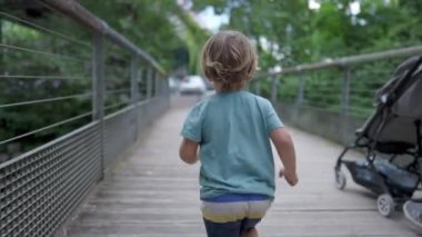 One active small boy running outdoors at park crossing bridge. Back of child runner in slow motion outside exercising. Sportive kid