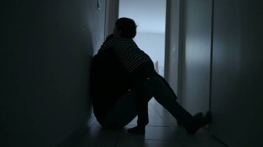 Child consoling depressed mother sitting in apartment corridor suffering from anxiety. Small son embracing mother during difficult times