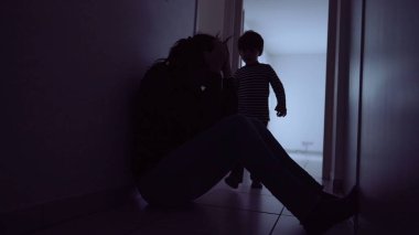 Child hugging mother suffering at home floor. Little boy silhouette consoling parent during depression. Single mother with kid