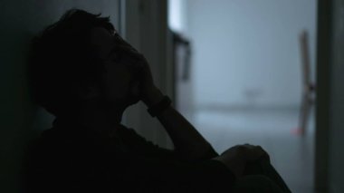 One depressed young man sitting on floor suffering from mental illness covering face with regret. Male person feeling anxious and depression