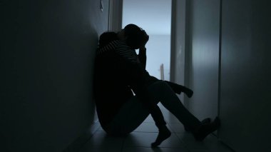 Child consoling depressed mother sitting in apartment corridor suffering from anxiety. Small son embracing mother during difficult times