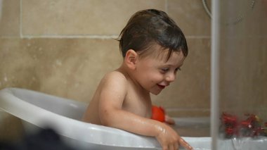 One happy little boy bathing inside small bathtub. Baby toddler bathing routine playing with toy. Childhood lifestyle