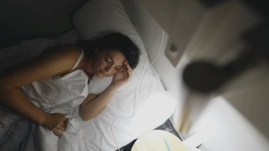 Woman turning bedside light ON in the middle of the night. Female person getting up early in the morning before sunrise