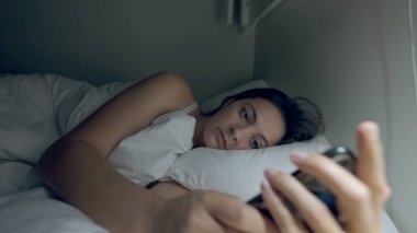 Woman staring at cellphone device at night in bed. Female person holding phone in the dark before sleep