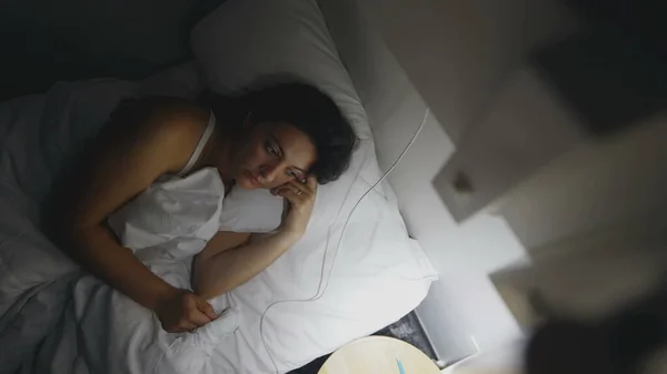 Pensive Woman laid in bed at night turns off lamp side. Thoughtful female person lying down going to sleep