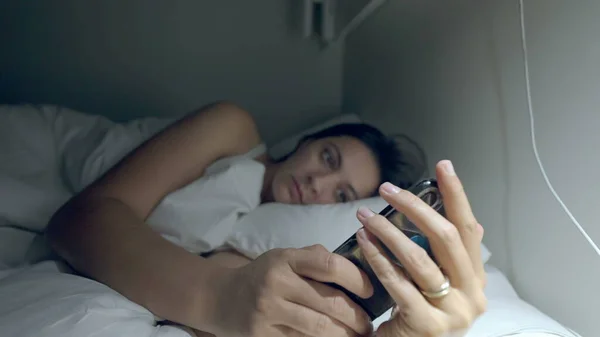 Woman staring at cellphone device at night in bed. Female person holding phone in the dark before sleep