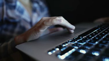 Closeup female hand using trackpag laptop at night. Person browses internet online in front of laptop screen