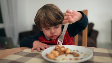Küçük mutlu çocuk çatalla tek başına yemek yiyor. Küçük bir çocuk kış mevsiminde kazak giyerek yemek yiyor.