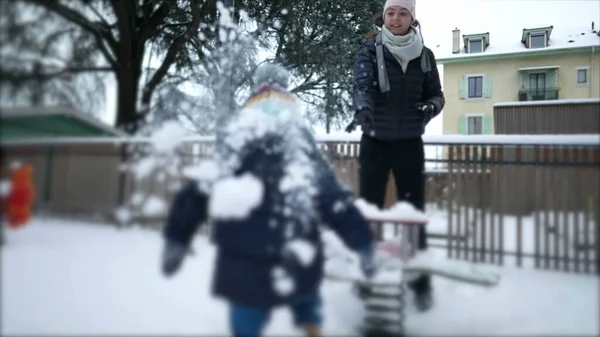 Mother throwing snowball to child. Parent and kid playing with snow. Mom throws snow ball battle